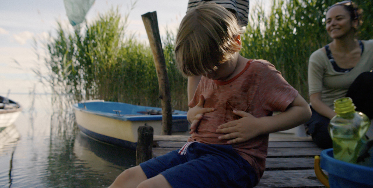 เด็กน้อยนั่งริมทะเลสาบทำให้เสื้อยืดสกปรก